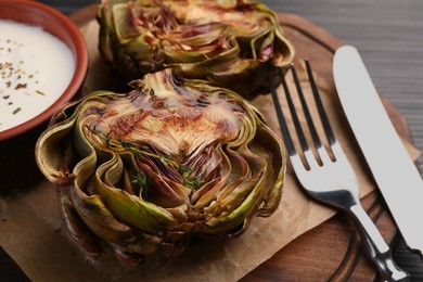 Photo of Tasty grilled artichoke and sauce on dark table, closeup
