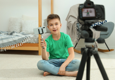 Photo of Cute little blogger with phone and selfie stick recording video at home