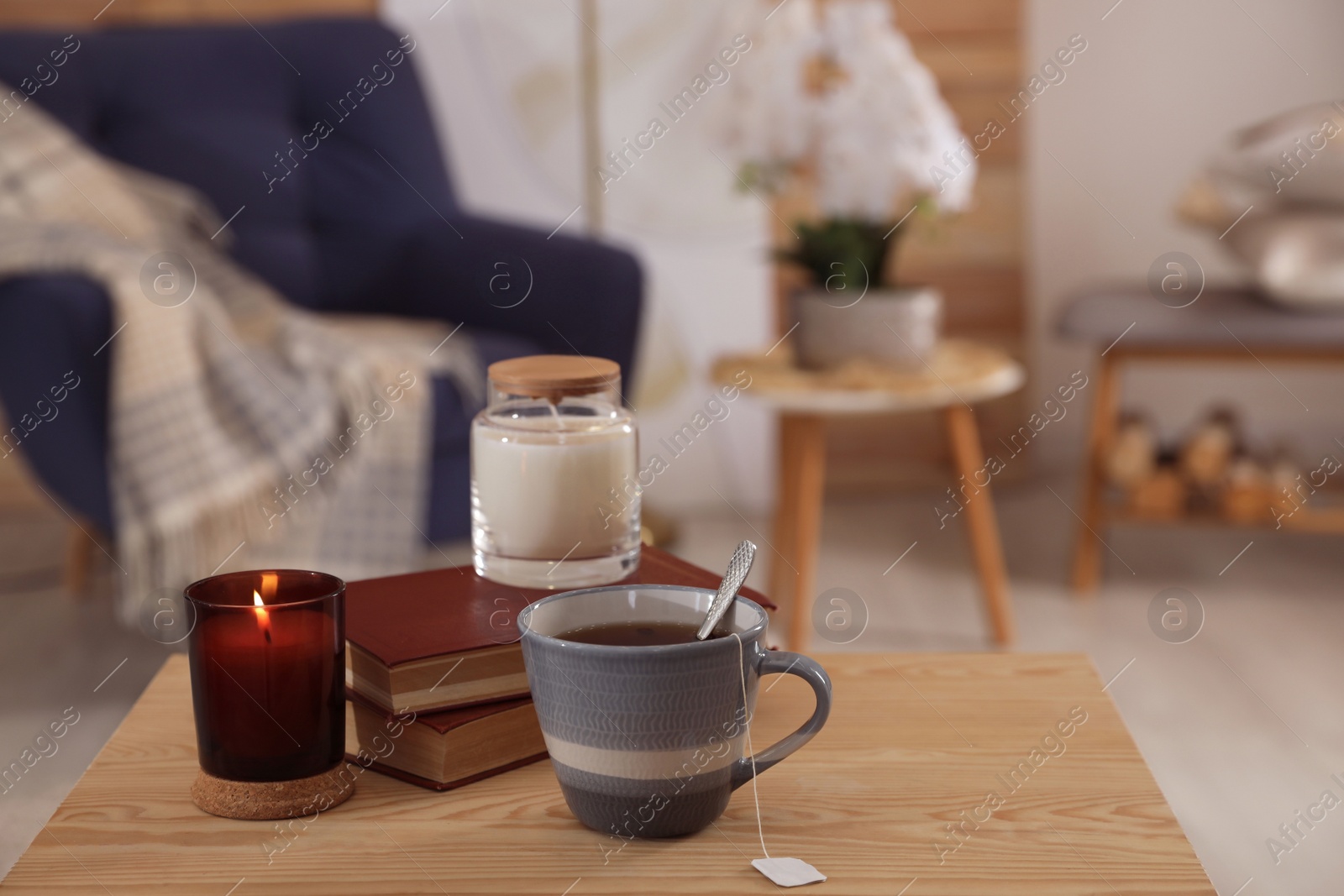 Photo of Cup of tea, books and candles on wooden table in living room. Interior design