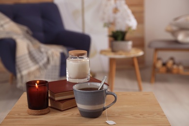 Photo of Cup of tea, books and candles on wooden table in living room. Interior design