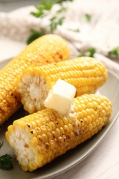 Fresh grilled corn cobs with butter on white wooden table, closeup