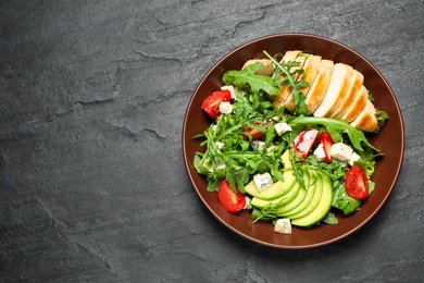 Photo of Delicious salad with chicken, arugula and avocado on black table, top view. Space or text