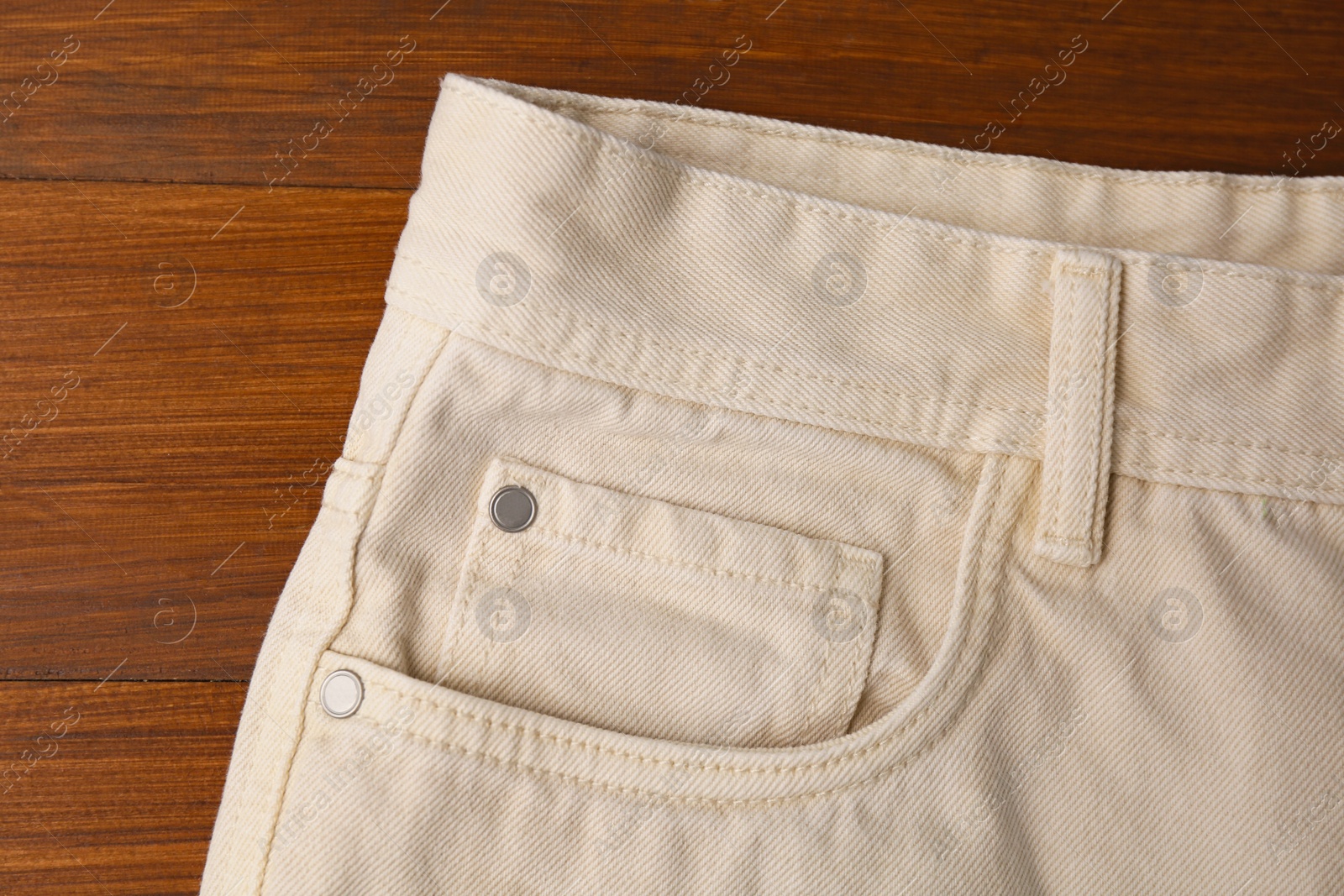 Photo of Stylish beige jeans on wooden background, closeup of inset pocket