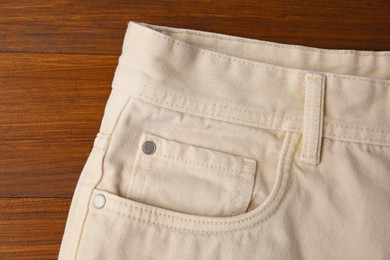 Photo of Stylish beige jeans on wooden background, closeup of inset pocket