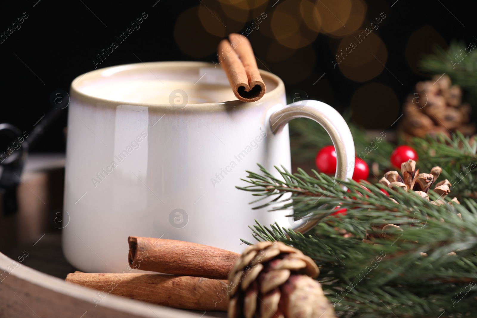 Photo of Tasty eggnog with cinnamon sticks against blurred lights, closeup