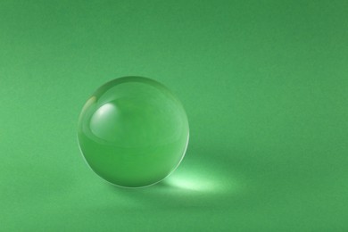 Photo of Transparent glass ball on light green background. Space for text