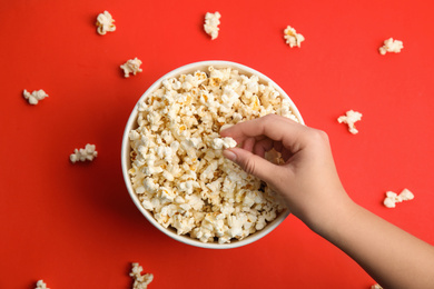 Woman taking fresh pop corn from bucket on red background, top view