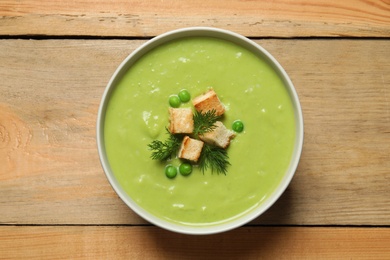 Photo of Fresh vegetable detox soup made of green peas with croutons in dish on wooden background, top view