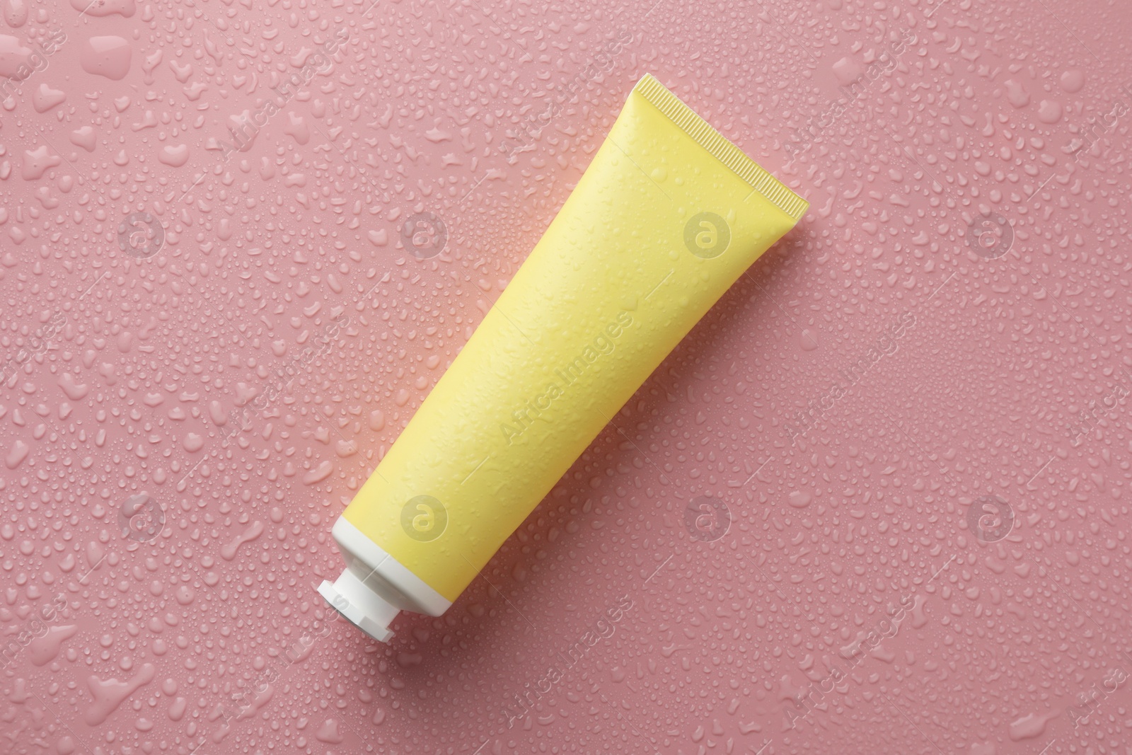 Photo of Moisturizing cream in tube on pink background with water drops, top view