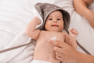 Photo of Woman applying body cream onto baby`s skin on bed, closeup