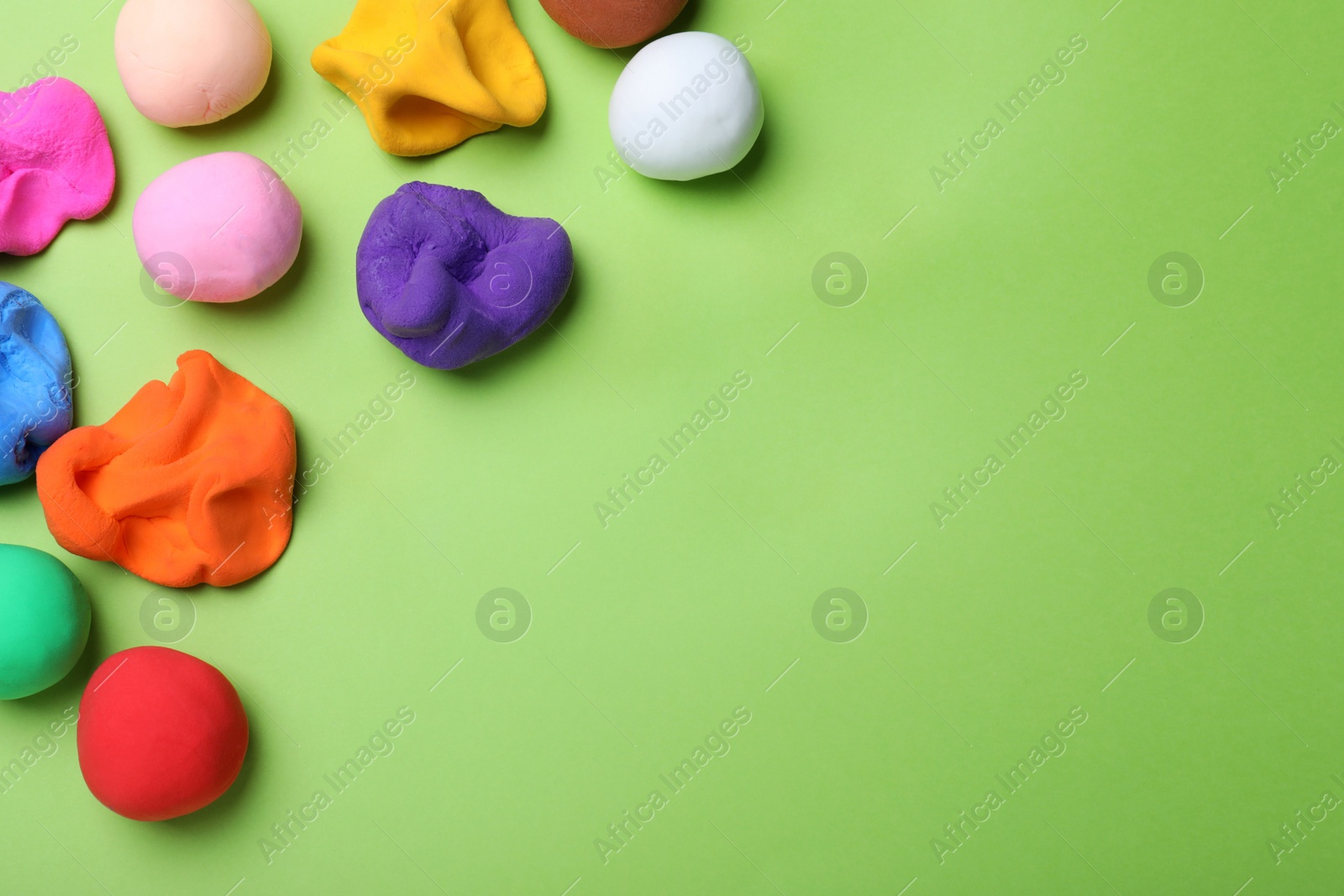 Photo of Colorful plasticine on green background, flat lay. Space for text