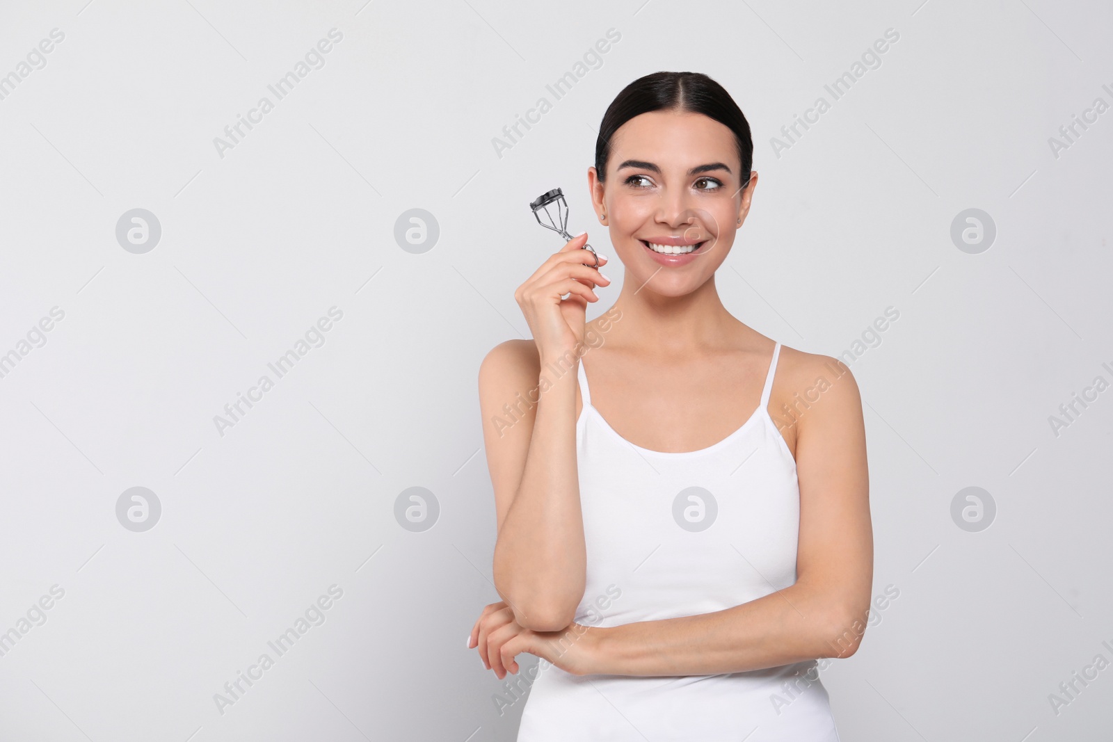 Photo of Beautiful young woman with eyelash curler on white background, space for text