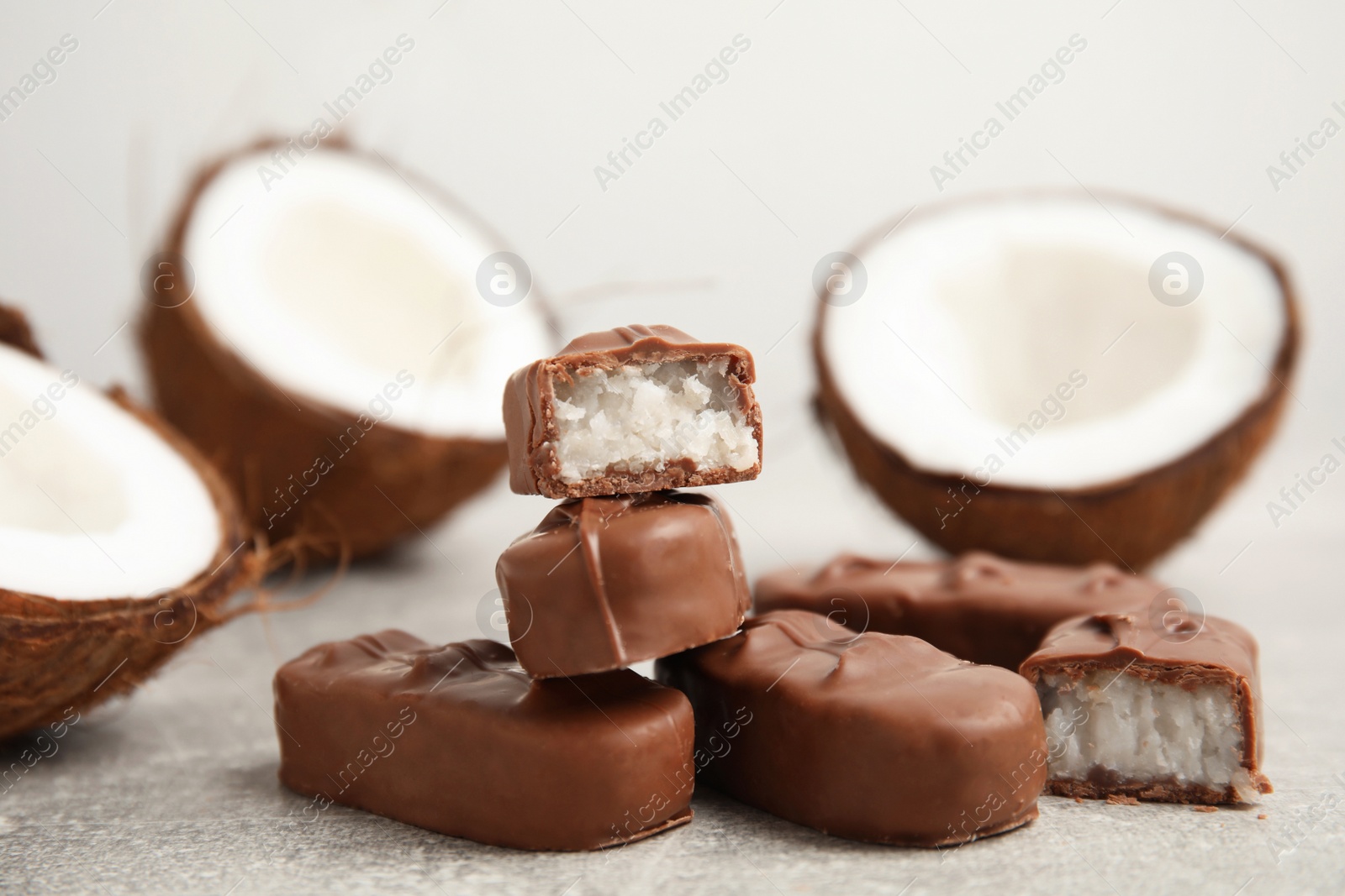 Photo of Delicious milk chocolate candy bars with coconut filling on grey table, closeup