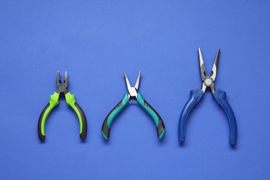 Photo of Different pliers on blue background, flat lay