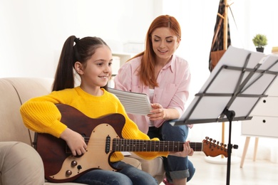 Photo of Little girl playing guitar with her teacher at music lesson. Learning notes