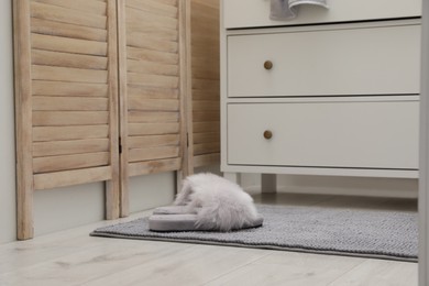 Photo of Grey bath mat with slippers near chest of drawers indoors