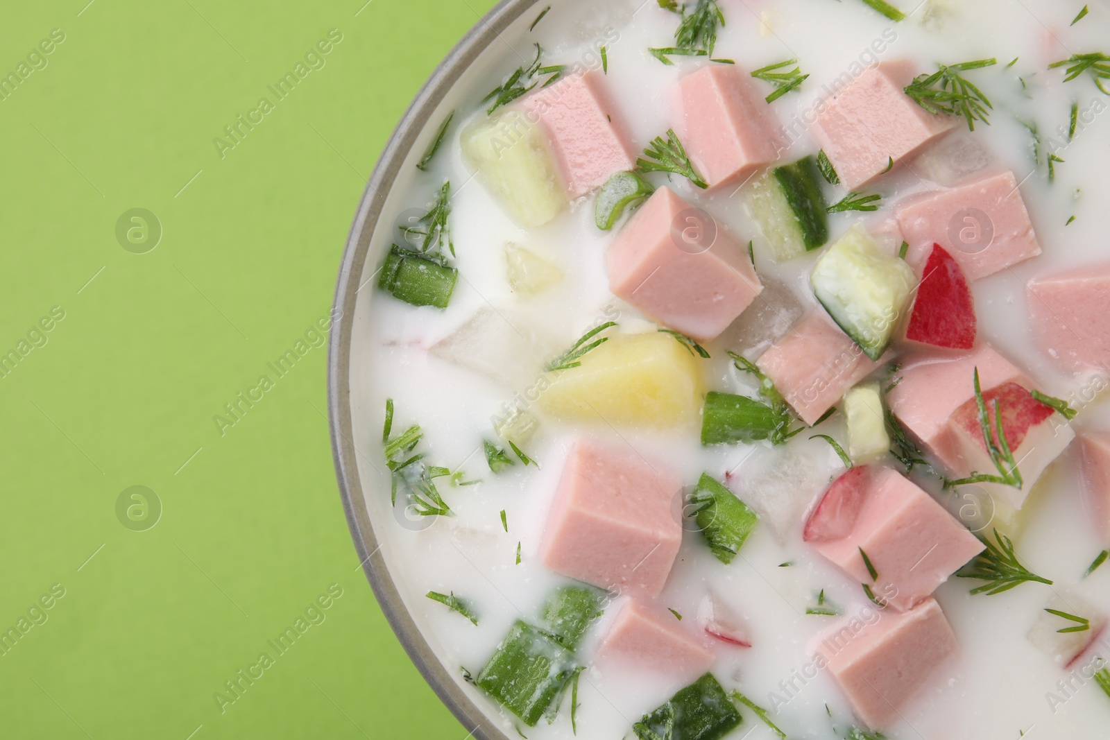 Photo of Delicious cold summer soup (okroshka) with boiled sausage in bowl on green table, top view. Space for text