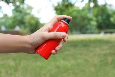 Photo of Woman with bottle of insect repellent spray outdoors, closeup