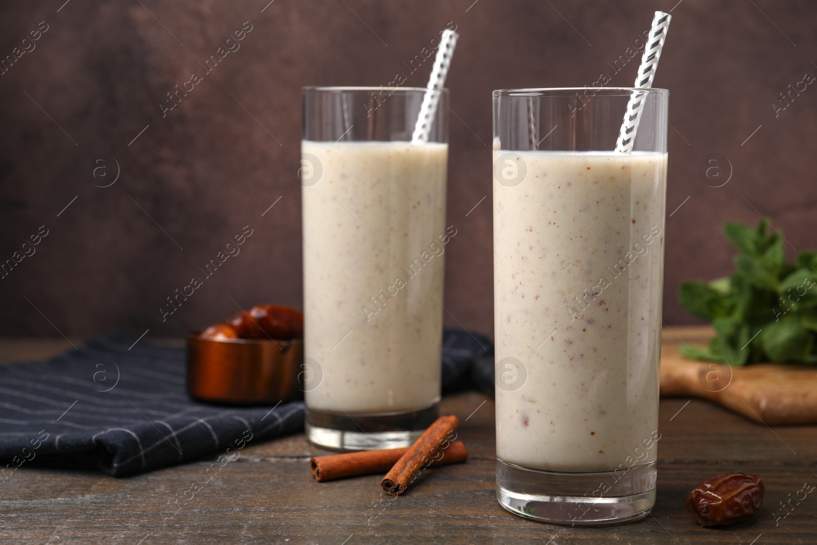 Photo of Glasses of delicious date smoothie, dried fruit and cinnamon sticks on wooden table, closeup. Space for text