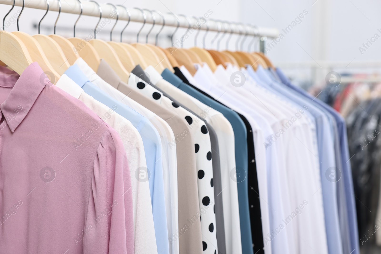 Photo of Dry-cleaning service. Many different clothes hanging on rack indoors, closeup