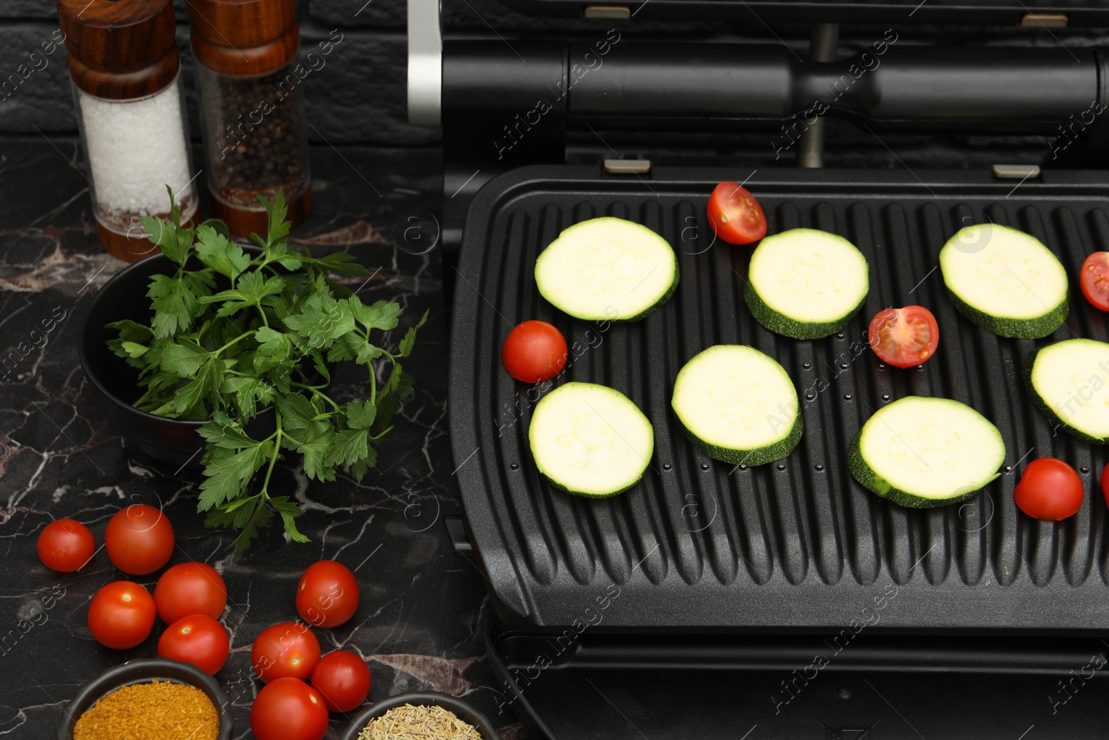 Photo of Electric grill with vegetables and spices on black marble table