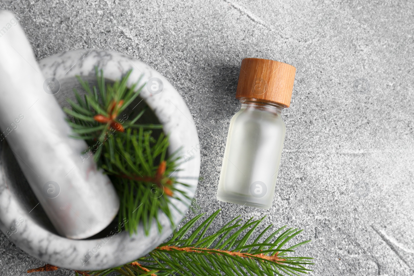 Photo of Bottle of aromatic essential oil and mortar with pine branch on light grey table, flat lay