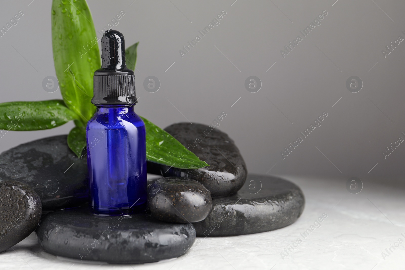 Photo of Bottle of face serum and spa stones on wet table against grey background. Space for text