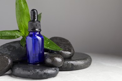 Bottle of face serum and spa stones on wet table against grey background. Space for text