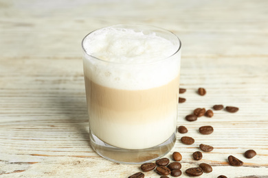 Photo of Delicious latte macchiato and coffee beans on white wooden table