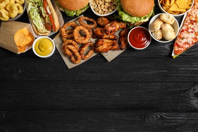 Photo of Burgers, onion rings and other fast food on black wooden table, flat lay with space for text