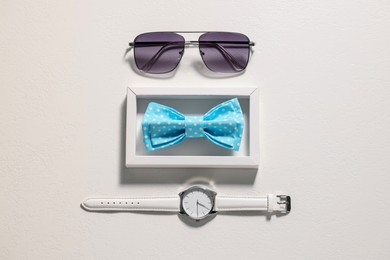 Stylish light blue bow tie, sunglasses and wristwatch on white background, flat lay
