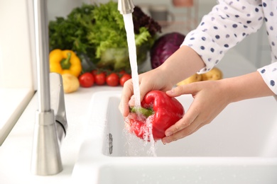 Woman washing fresh red bell pepper in kitchen sink, closeup