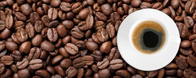 Image of Cup of tasty aromatic coffee on roasted beans, top view. Banner design