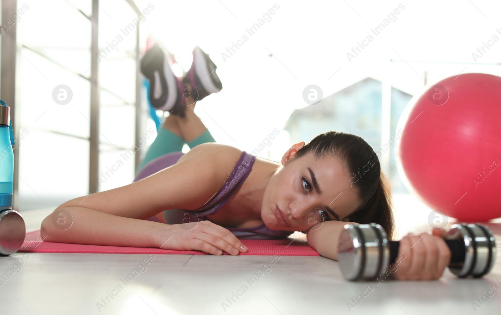 Photo of Lazy young woman with dumbbell lying on yoga mat indoors