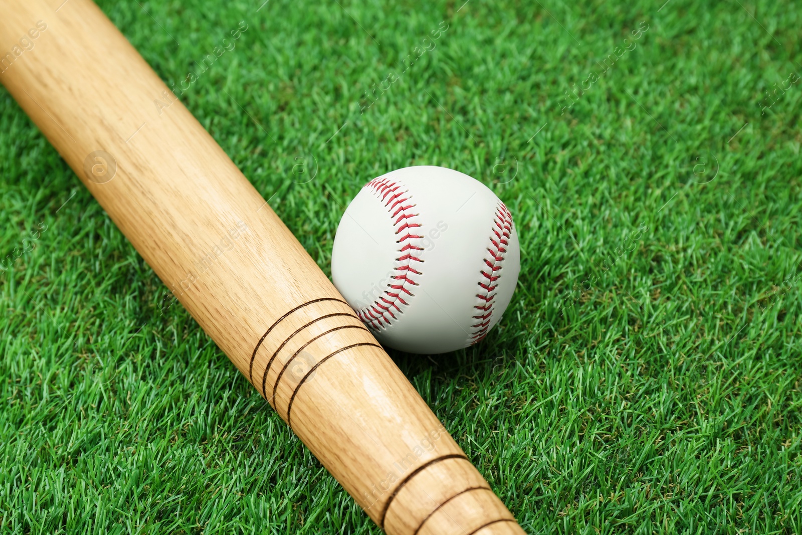 Photo of Wooden baseball bat and ball on green grass, closeup. Sports equipment