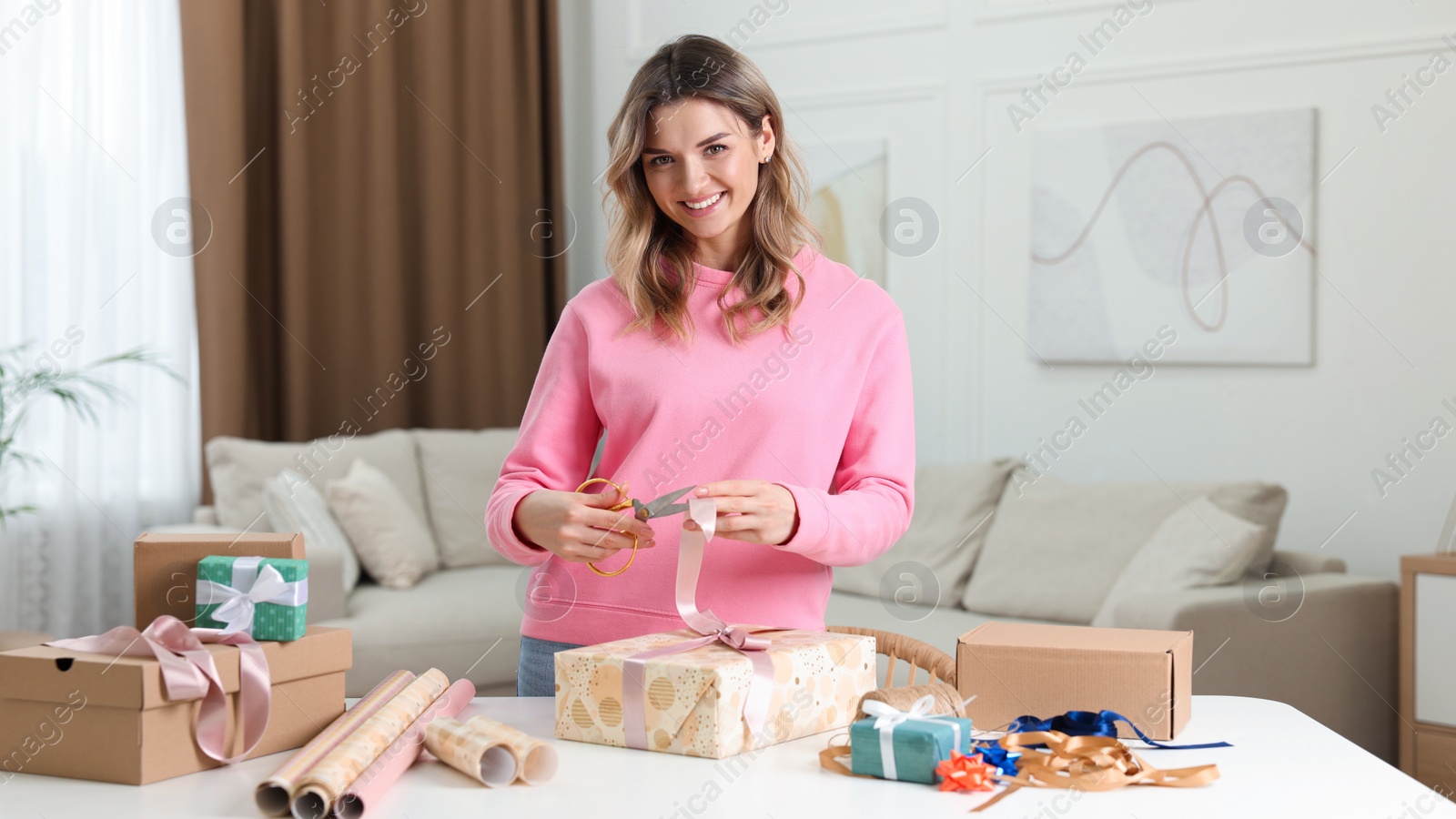 Photo of Beautiful young woman wrapping gift at table in living room