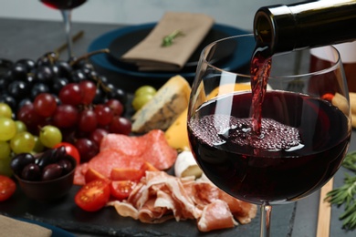 Photo of Pouring red wine into glass on served table, closeup. Space for text