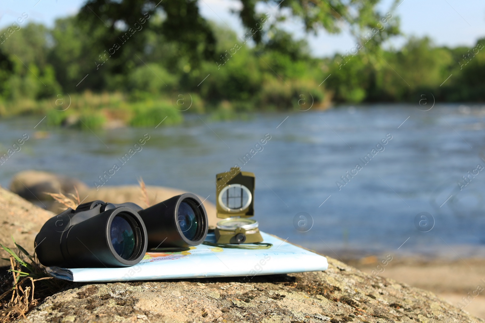 Photo of Binoculars, compass and map on stone near river, space for text. Camping equipment