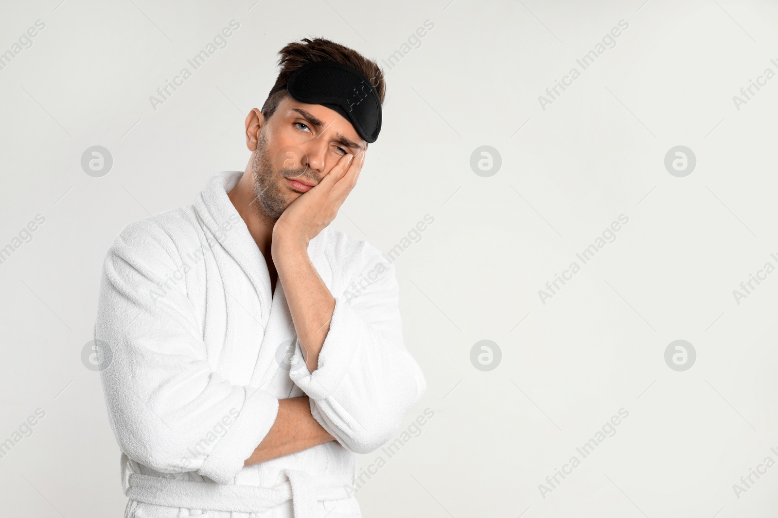 Photo of Sleepy young man in bathrobe on white background