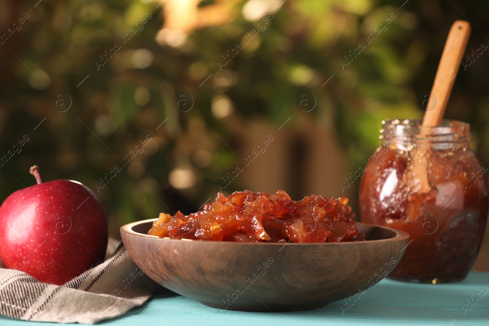 Photo of Delicious apple jam and fresh fruit on light blue wooden table against blurred background, closeup. Space for text