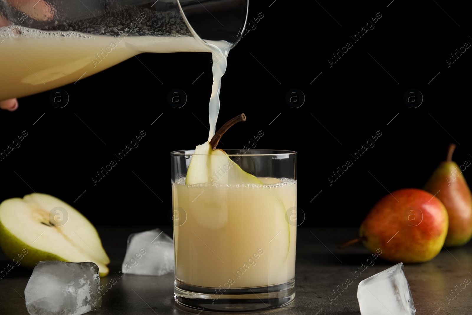 Photo of Pouring tasty pear juice into glass on grey table with ice cubes, closeup