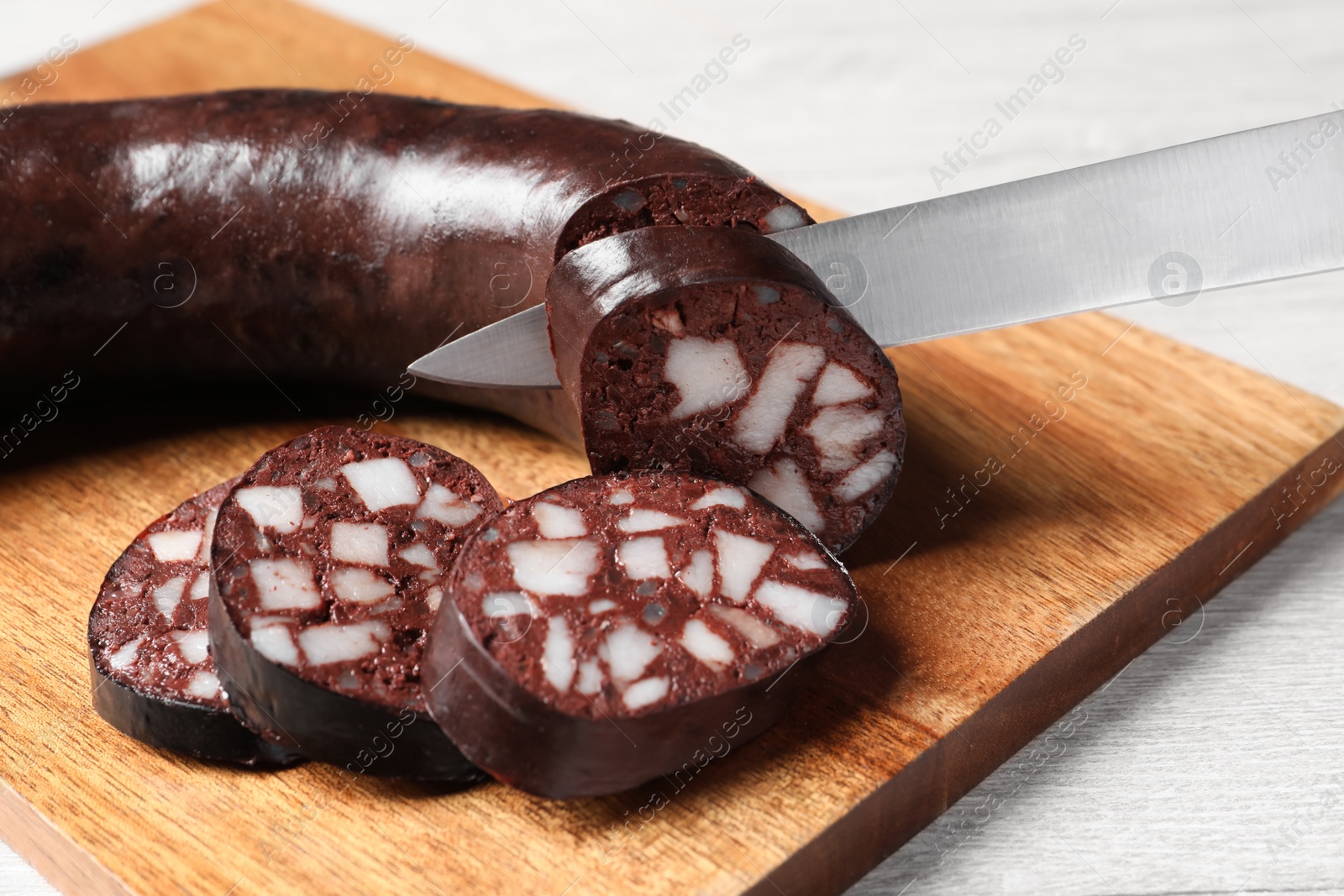 Photo of Cutting tasty blood sausage on white table, closeup