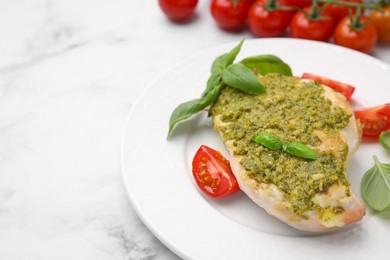 Photo of Delicious chicken breast with pesto sauce, tomatoes and basil on white marble table, closeup. Space for text