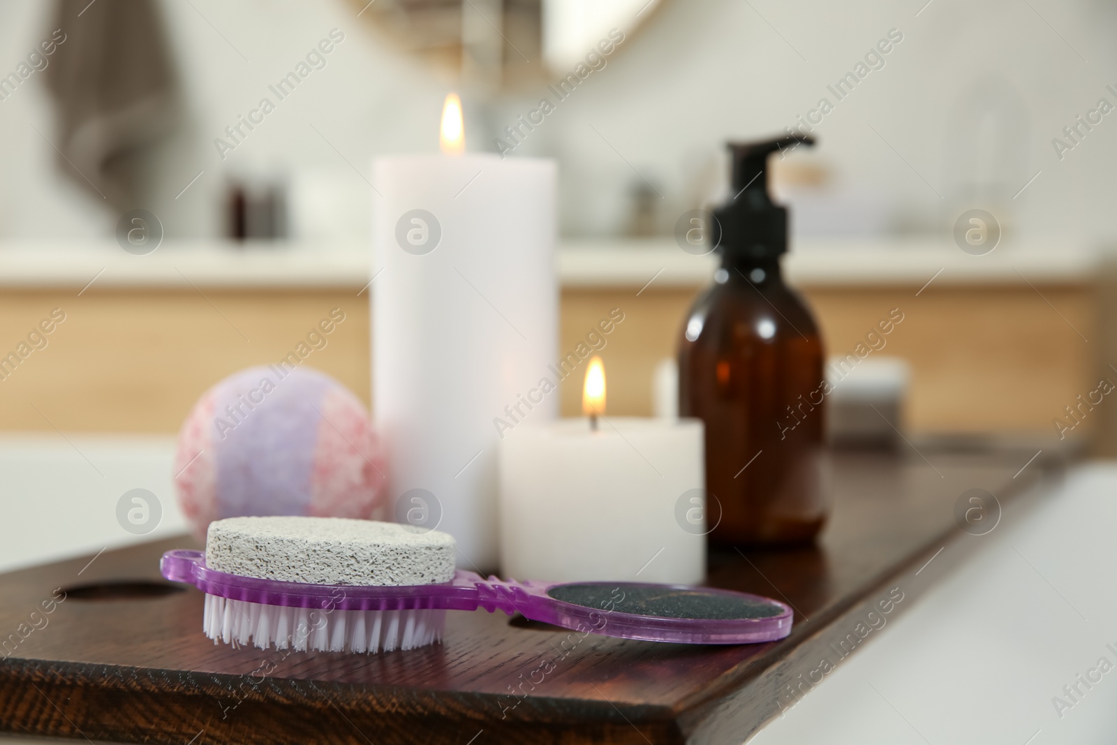 Photo of Pedicure tool with pumice stone and foot file near burning candles on wooden caddy in bathroom