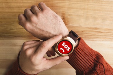 Man using SOS function on smartwatch at wooden table, closeup