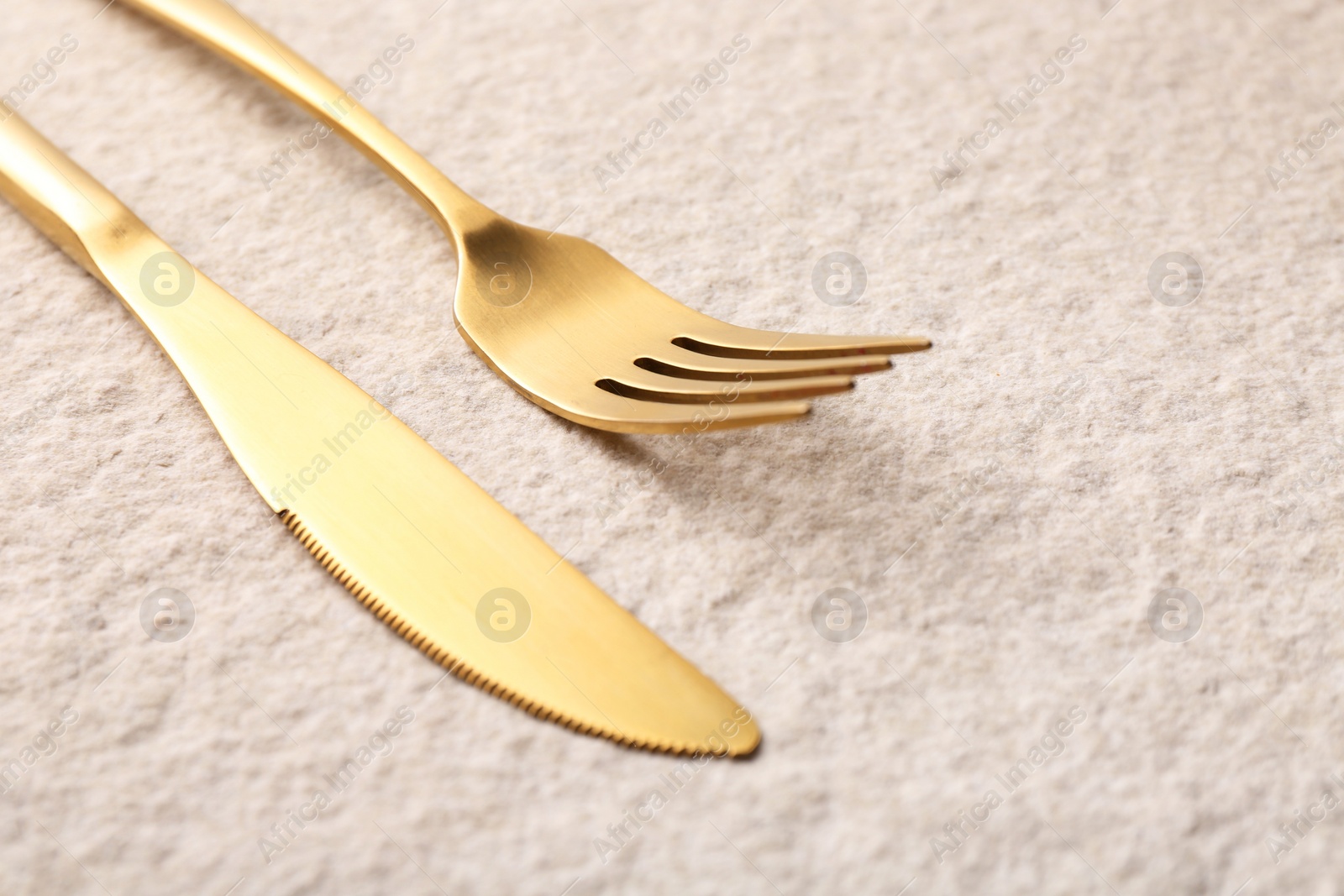 Photo of Stylish cutlery. Golden knife and fork on light textured table, closeup