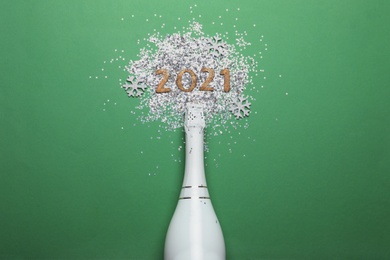 Photo of Year number 2021, bottle with champagne and shiny confetti on green background, flat lay