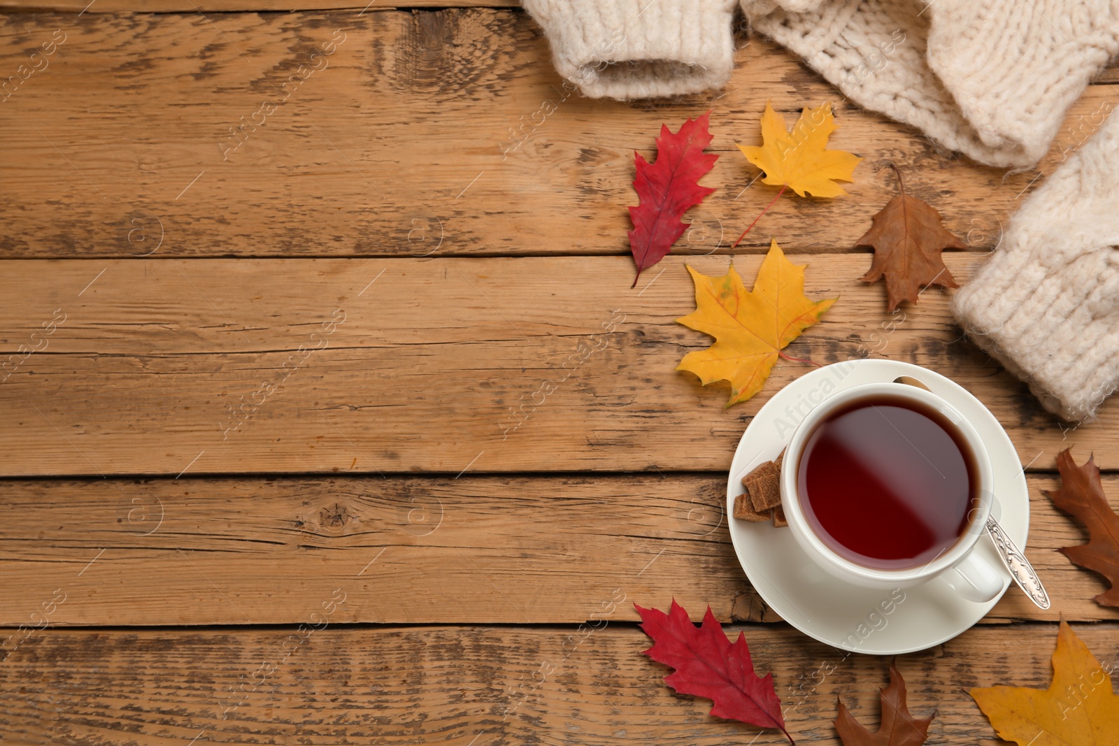 Photo of Cup of hot tea, sweater and autumn leaves on wooden table, flat lay. Space for text