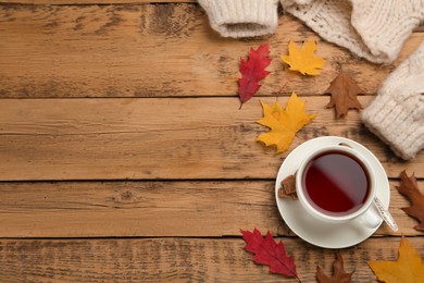 Cup of hot tea, sweater and autumn leaves on wooden table, flat lay. Space for text
