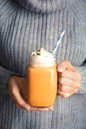 Photo of Woman in knitted sweater holding mason jar with pumpkin spice latte and whipped cream, closeup